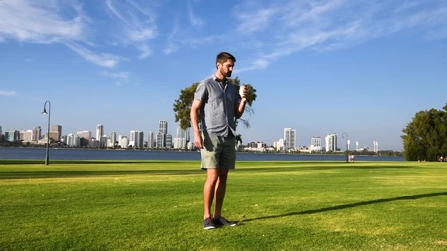 Caucasian man with beard deliberately drops trash in green park, wide shot