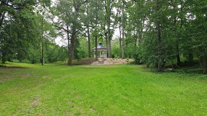 Obraz premium Wooden little arbor in a wooded park in the summer. Latvia, July 2019