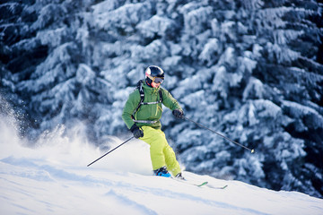 Fototapeta na wymiar Proficient skier coming down along wooded hillside using professional ski equipment and making deep snow powder. Winter outdoors activities concept. Picturesque forest scenery on background. Side view