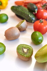 Kiwi fruit, cucumbers and red tomatoes on white table