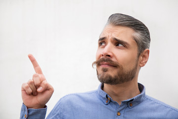 Closeup of positive focused man pointing finger away at copy space. Grey haired young man in blue casual shirt posing isolated over white background. Advertising concept