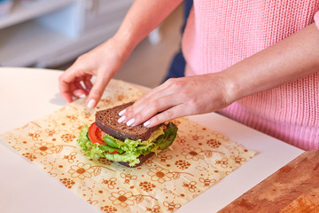 Woman hands wrapping a healthy sandwich in beeswax food wrap - obrazy, fototapety, plakaty