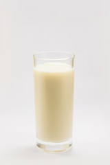A cup of soy milk stands alone on a pale yellow background.