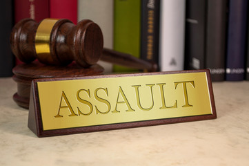 Golden sign with engraved word assault with gavel on a desk