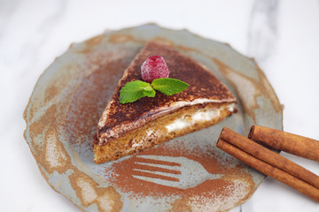 Piece of cake with raspberry and mint leaves on top, decorated with cinnamon and cacao, served on stylish plate