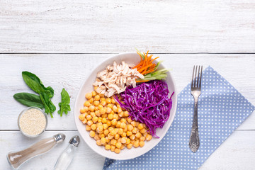 Poke bowl with chickpeas, steamed chicken, cabbage, carrots and cucumber on a white wooden background. Healthy eating concept.