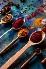 Spoons with spices on a colored concrete background