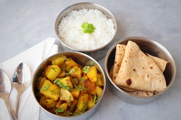 Stainless steel Lunch Box or Tiffin with Indian food menu Chapati or Roti, Garlic Dal Tadka, White Rice and Potato or Jeera aloo. with spoons, tissue paper and glass of water. Copy space