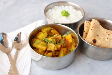 Stainless steel Lunch Box or Tiffin with Indian food menu Chapati or Roti, Garlic Dal Tadka, White Rice and Potato or Jeera aloo. with spoons, tissue paper and glass of water. Copy space