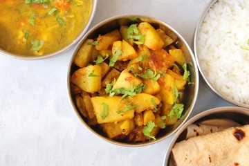 Stainless steel Lunch Box or Tiffin with Indian food menu Chapati or Roti, Garlic Dal Tadka, White Rice and Potato or Jeera aloo. with spoons, tissue paper and glass of water. Copy space
