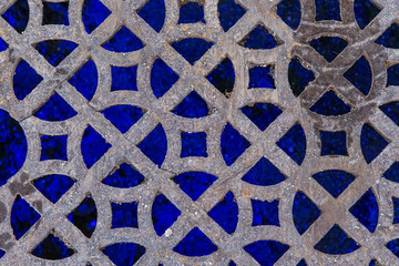 A geometric metal drainage cover illuminated at night