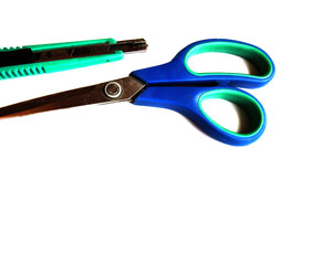 Green stationery knife and blue scissors on a white isolated background. Place for text.
