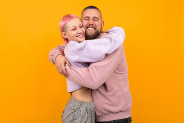 Unusual pretty woman with short pink hair and tattoo hugs with her boyfriend isolated on orange background