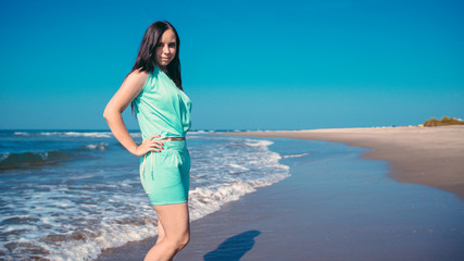 Stylish woman near waving sea. Adult female in trendy summer outfit smiling and looking at camera while standing against waving sea and cloudless blue sky on resort