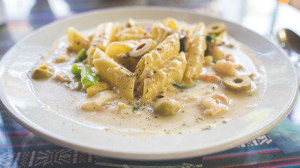 Yummy pasta on cafe table. Closeup plate with portion of tasty pasta with cream sauce placed on table in restaurant