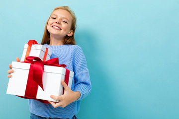 Little caucasian girl holds a white boxes with gifts and rejoices isolated on blue background