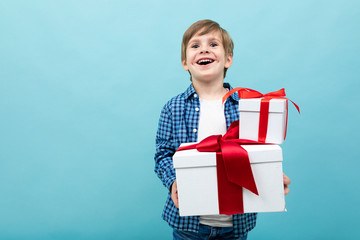 Caucasian boy holds many white boxes with gifts and rejoices, portrait isolated on blue background