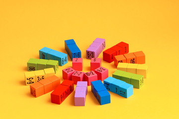 Naklejka premium Multicolored wooden cubes with a multiplication table on the sides. Laid out in the shape of a smiling sun, on a yellow monochrome isolated background. Copy space. School education. Selective focus.