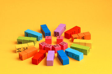 Multicolored wooden cubes with a multiplication table on the sides. Laid out in the shape of a smiling sun, on a yellow monochrome isolated background. Copy space. School education. Selective focus.