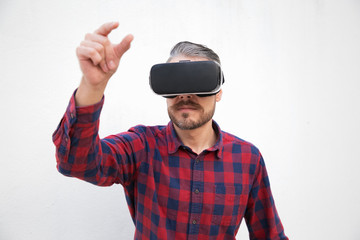 Focused bearded man in virtual reality headset. Handsome focused bearded men checkered shirt using virtual headset and moving hand on grey background. Technology concept