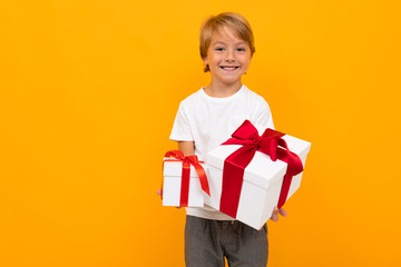Caucasian boy holds many white boxes with gifts and rejoices, portrait isolated on yellow background