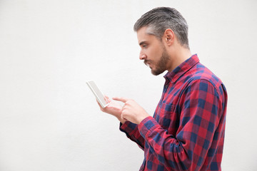 Side view of serious bearded man using tablet pc. Concentrated bearded man in checkered shirt design digital tablet on grey background. Wireless technology concept