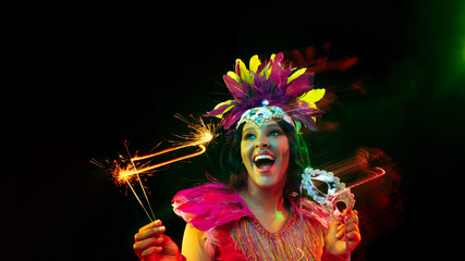 Beautiful young woman in carnival mask, stylish masquerade costume with feathers and sparklers...
