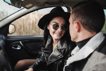 Obraz na płótnie Canvas Happy Traveling Couple Dressed in Black Stylish Clothes Enjoying a Road Trip Sitting Inside the Car, Vacation Concept
