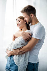 handsome man hugging attractive and smiling woman in apartment