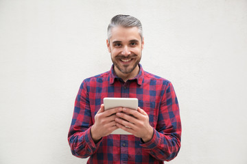Cheerful bearded man with tablet pc. Front view of handsome happy man holding tablet computer and smiling at camera. Wireless technology concept