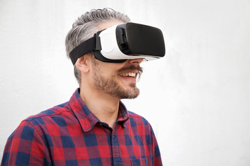 Close-up view of cheerful man in VR headset. Handsome happy bearded man in checkered shirt using virtual reality headset on grey background. Technology concept