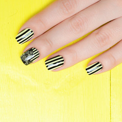 Bright yellow manicure with black stripes and sunflowers pattern on yellow background