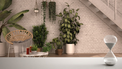 White table or shelf with crystal hourglass measuring the passing time over modern conservatory, winter garden, lounge with armchair, interior design, copy space background