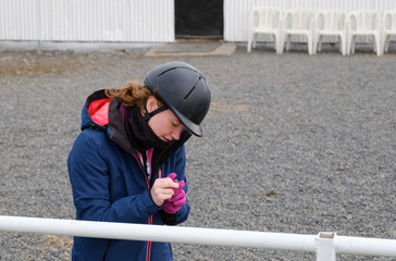 Girl puts on pink gloves before she goes horse riding, total focus on gloves, she wears a riding cap, Blönduós, Iceland