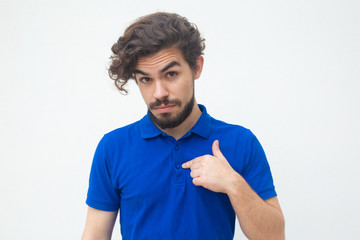 Surprised guy pointing finger at himself with questioning face. Handsome bearded young man in blue...