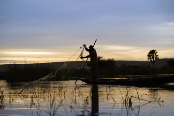 Silhouette Of A Malian Fisherman Hauling His Net Into His Boat On The Niger River At Sunset - obrazy, fototapety, plakaty