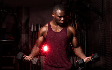 Fototapeta na wymiar Muscular African American male bodybuilding athlete does dumbbell curls in a dark grungy gym with dramatic lighting flare 