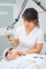 medical salon woman employee uses effective neodymium laser removing unwanted scars on young patient face