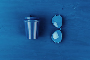 Top view of takeaway coffee cup with aviator sunglasses on classic blue background
