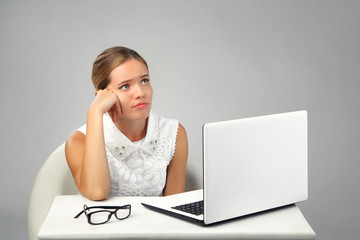 sad tired girl sitting at a table with a laptop. Waiting for the end of the working day