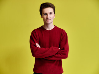 Portrait of a handsome young man with a short haircut in a burgundy sweater on a yellow background....