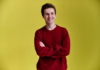 Portrait of a handsome young man with a wide smile. Caucasian short-haired man in a burgundy sweater on a yellow background. Cute looks at the camera, standing straight.