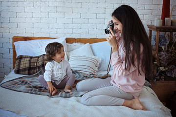 Happy loving family. Mother playing with her daughter child girl on the bed and and photographing her.