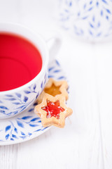 Pink fruit tea and homemade cookie star with jam on a white wooden background