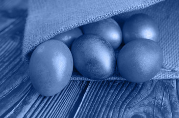 Colored Easter eggs on a wooden background in burlap, toned trendy classic blue color of year 2020
