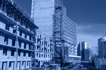 Crane and building construction site against blue sky, toned trendy classic blue color of year 2020