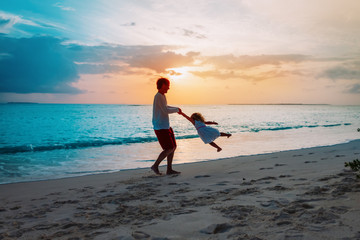 Father and little daughter silhouettes play at sunset beach