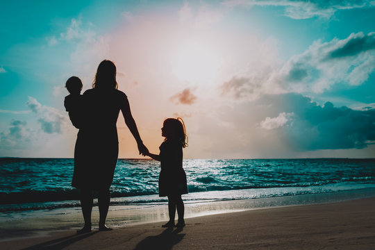 Mother With Two Kids Walking On Beach At Sunset