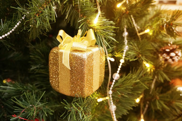 Solf focus of christmas tree decoration. Golden gift box hanging on the branches of a Christmas tree, Christmas background with festive decorations.