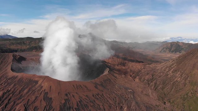 Aerial shot of smoking Mount Bromo, moving towards Batok crator in the background, horizon view, moving towards Batok crater, showing flanks of Bromo. Java, Indonesia